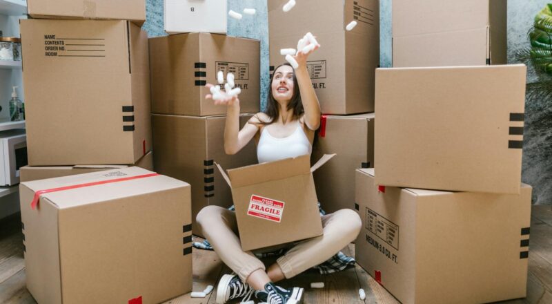 Woman in Black Tank Top Sitting on Brown Cardboard Box