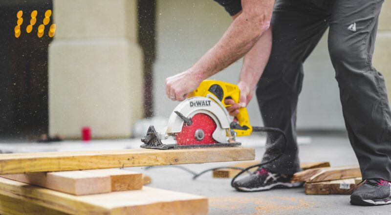 man in black sweatpants using DEWALT circular saw and cutting a wood plank