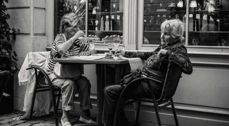 grayscale photo of two woman sitting beside the table